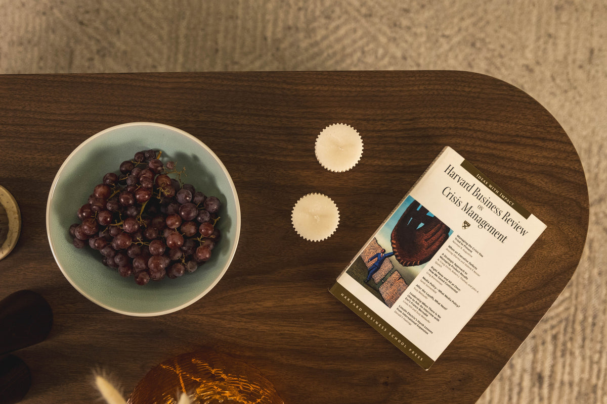 A walnut tabletop from above — a bowl of grapes, hand-carved candle cups and a book resting on the grain